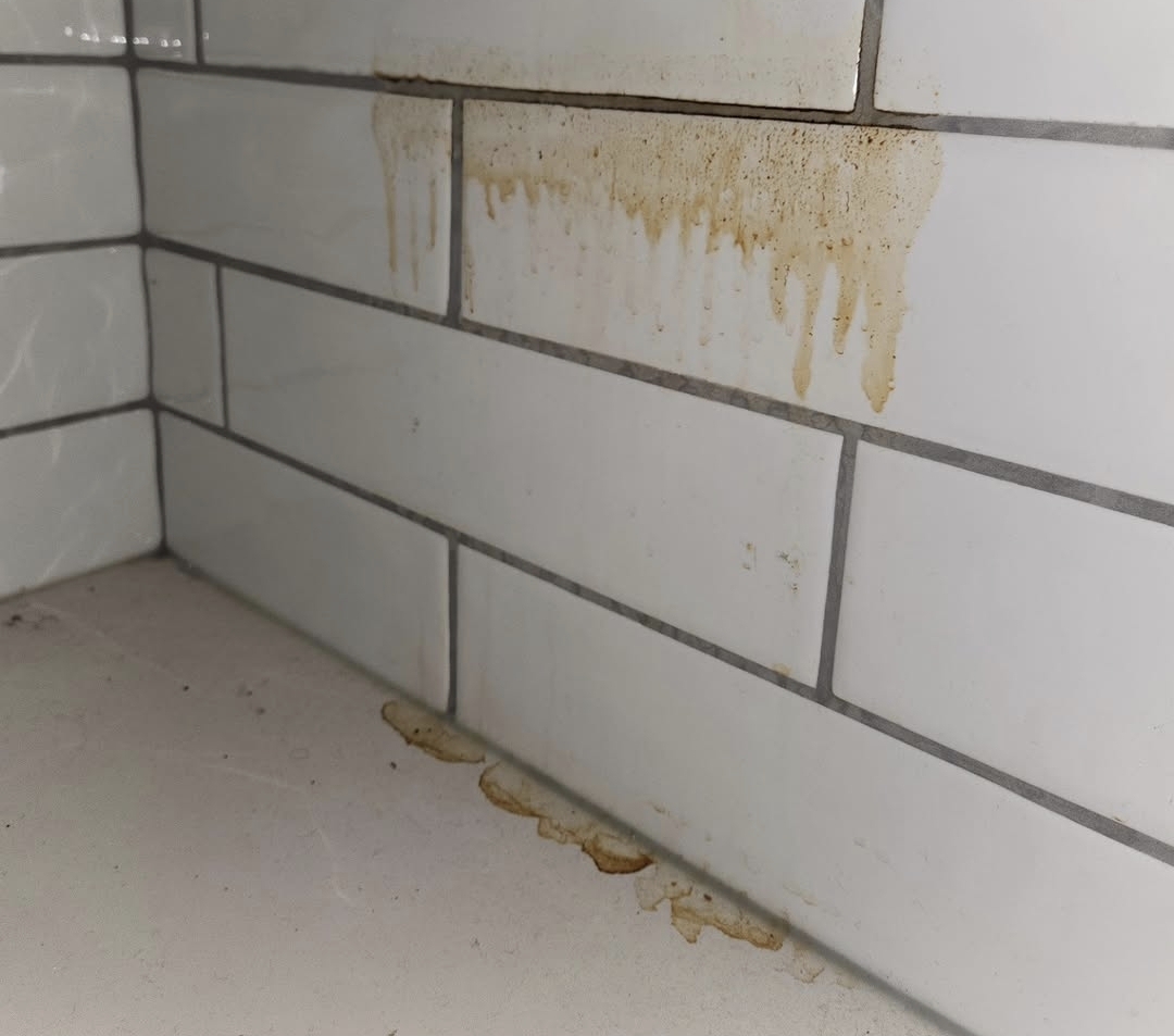 White subway tile shower corner with brown rust drip stains before cleaning