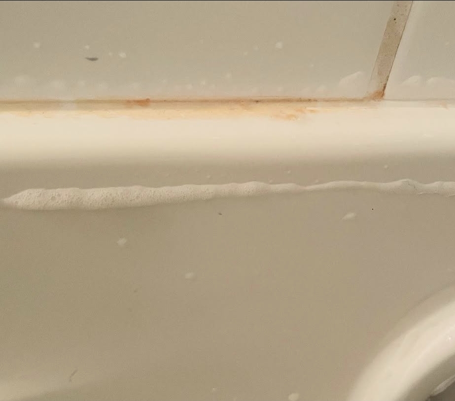 Bathtub edge with rust stains and soap scum before cleaning